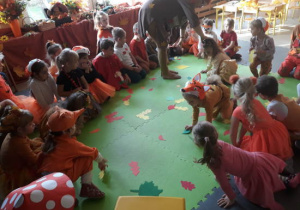 Dzieci siedzące w kole. W środku na dywanie kolorowe liście.